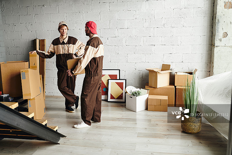 两个年轻的装卸工穿着工作服，一边帮着搬到新公寓，一边送纸箱图片素材