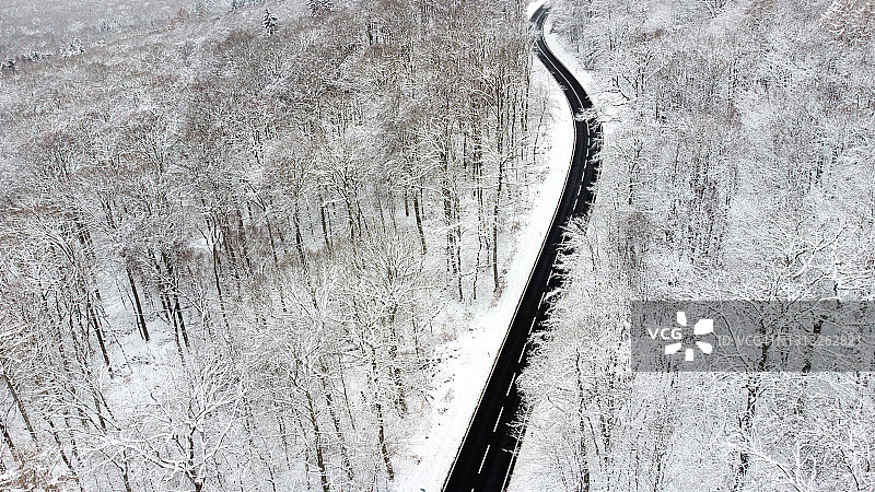 道路穿过积雪覆盖的森林-鸟瞰图。图片素材