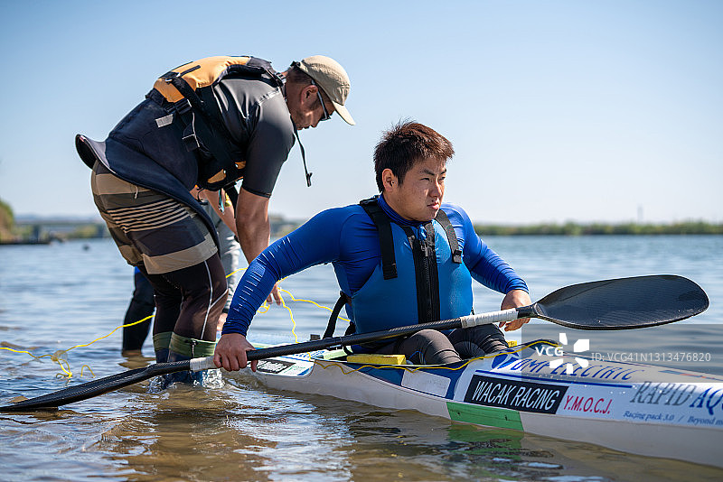 两名教练协助一名截瘫运动员进入皮划艇进行独木舟训练。图片素材