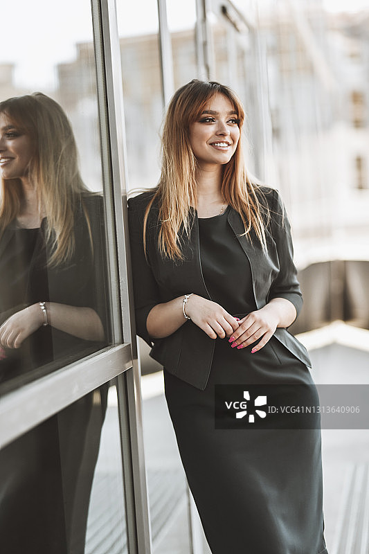微笑优雅的女商人倚在办公楼窗外图片素材