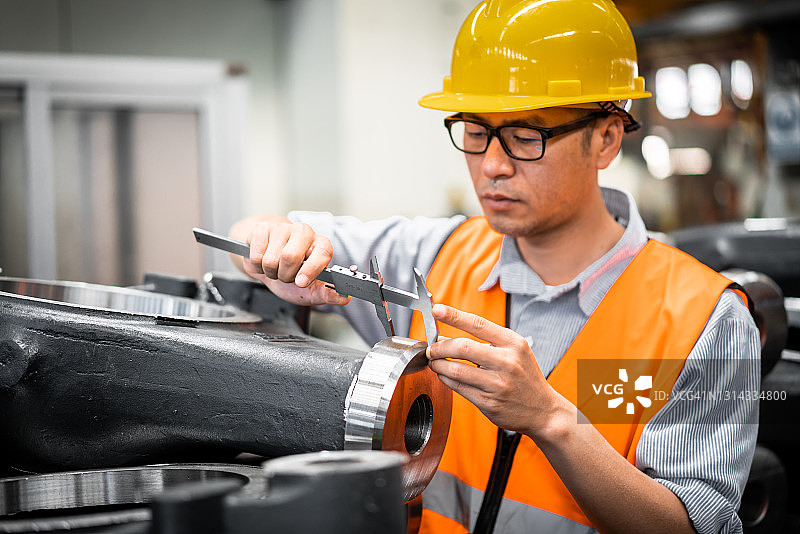 一名亚洲男性蓝领工人在工厂测量零件图片素材