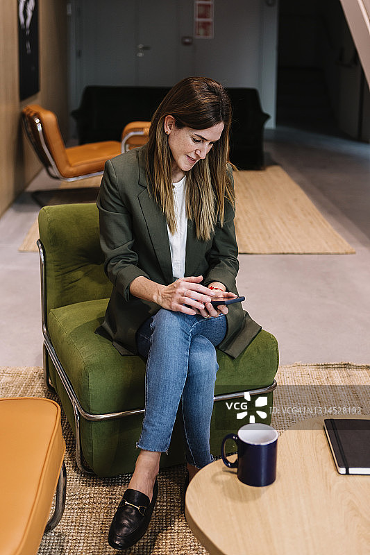 女企业家坐在办公室沙发上使用智能手机图片素材