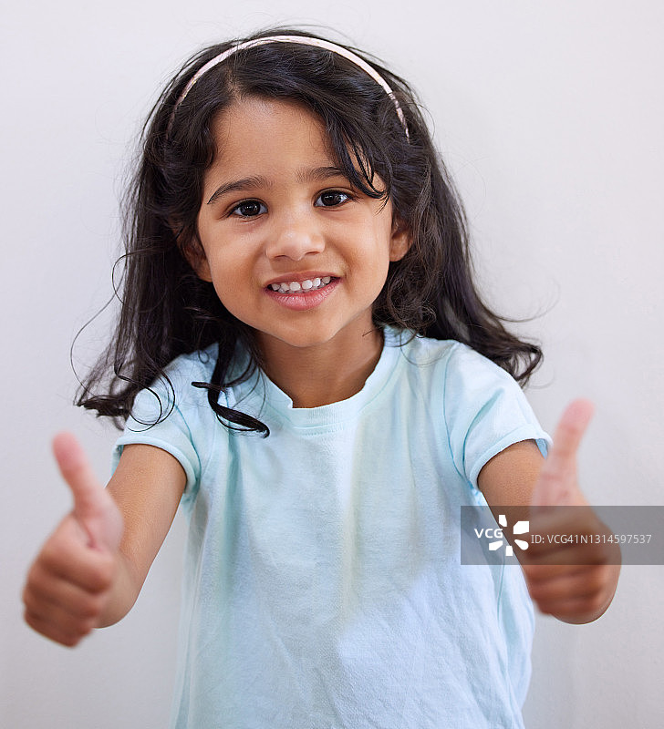 一个可爱的小女孩对着墙摆姿势，竖起大拇指图片素材