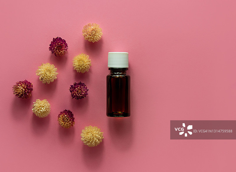 草本精油玻璃瓶模型粉色花朵背景。替代医学皮肤护理水疗芳香疗法图片素材