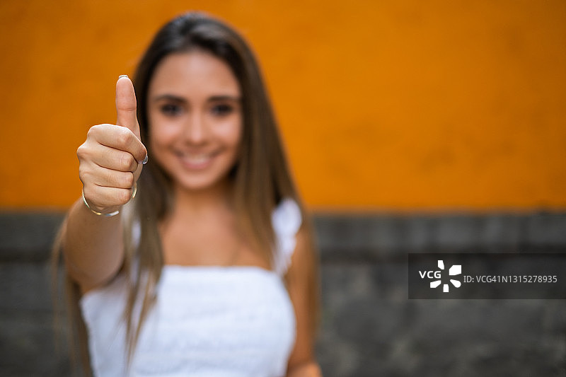 在墨西哥城，一位年轻的西班牙妇女看着镜头，竖起大拇指，专注于手图片素材