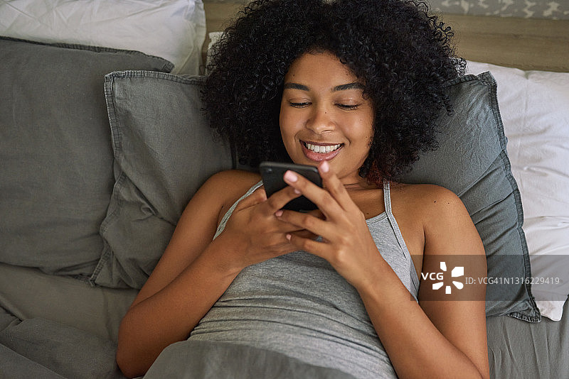 一张年轻女子躺在床上使用手机的照片图片素材