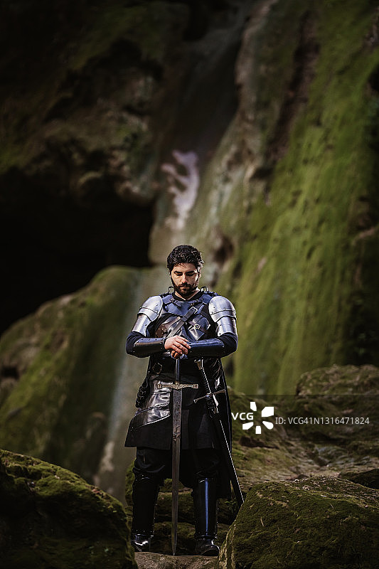 准备了神秘的黑色幻想骑士站在苔藓覆盖的岩石前拿着他的剑图片素材