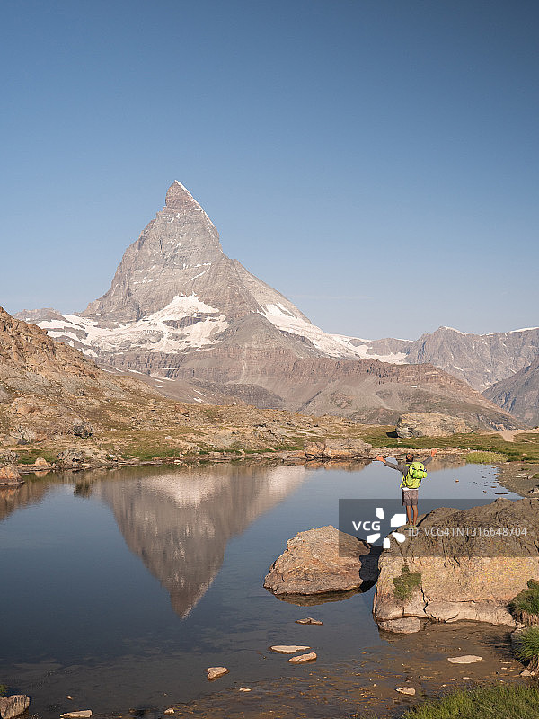 一名男子站在高山湖的岩石上，伸开双臂图片素材