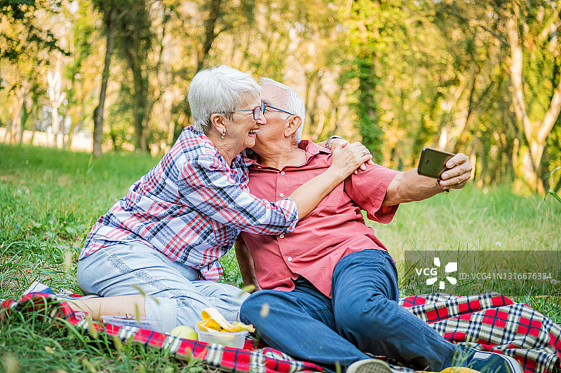 快乐的老年夫妇在公园里用智能手机自拍合影图片素材
