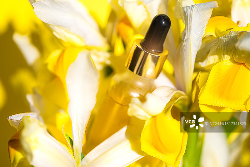 时尚的美容概念，化妆瓶中的血清与滴管和黄色和白色的花朵。图片素材