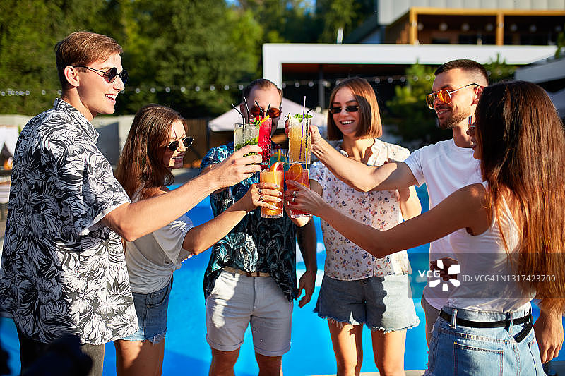 一群朋友有乐趣的池畔夏季派对，碰杯与五颜六色的夏季鸡尾酒户外酒店游泳池。人们在豪华别墅度假时喝新鲜的果汁图片素材