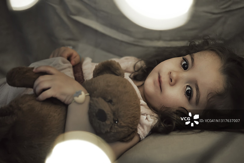 一个两岁的小女孩躺在她的泰迪熊旁边图片素材