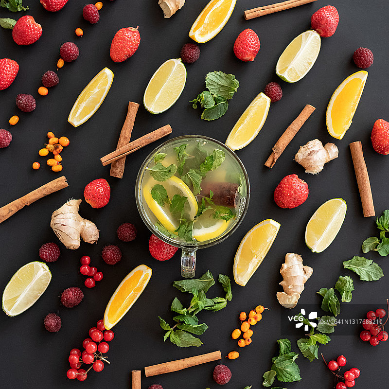 下午茶时间。图案的浆果，水果和香草，成分在黑色的背景和混合茶在玻璃杯在图像的中心。俯视图图片素材