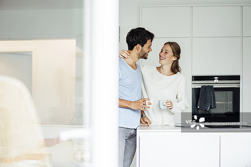 一对幸福的年轻夫妇站在厨房里看着对方图片素材