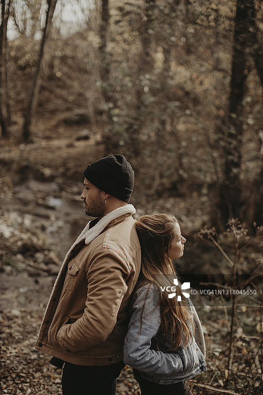 双手插在口袋里的夫妇背靠背站在森林里图片素材