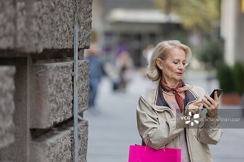 一位老妇人在逛完购物中心后走在城市的街道上。图片素材