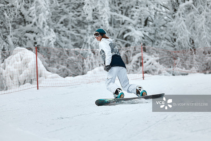 冬天在山上骑滑雪板的快乐女人。穿白色滑雪服的女人图片素材