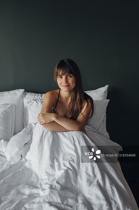 一个年轻美丽的女人坐在大床上的肖像在周末的早晨图片素材