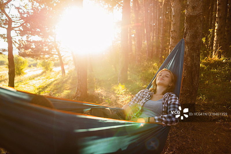 一位美丽的年轻女子正在树林里的吊床上休息图片素材