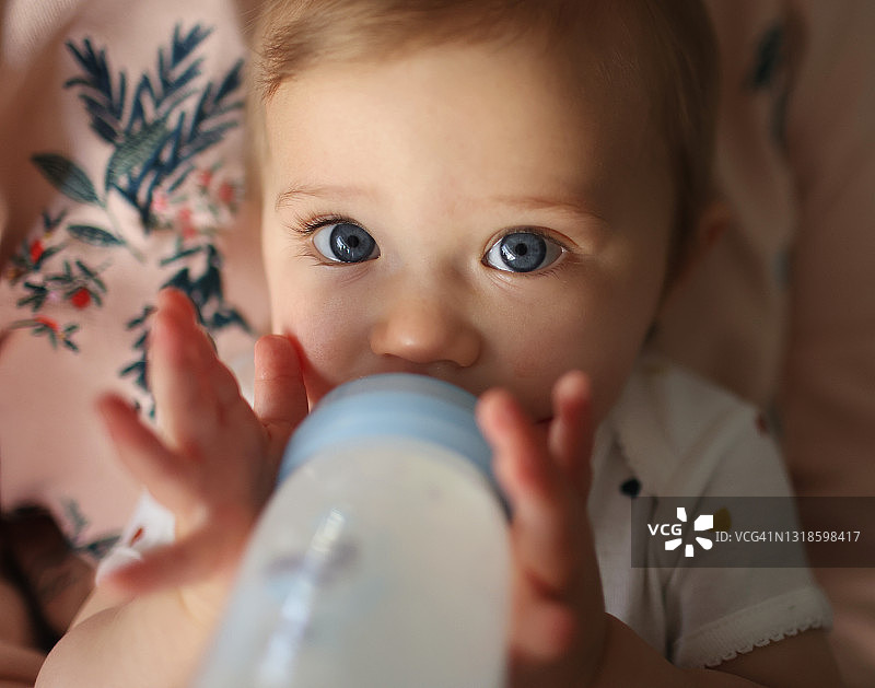 一个1岁的小女孩在她妈妈的怀里喝她的婴儿奶瓶图片素材