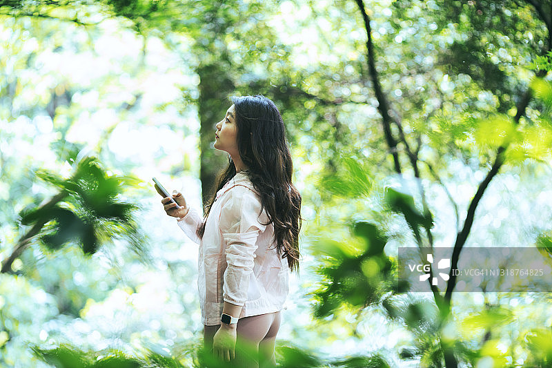 一名年轻女子在森林里使用智能手机图片素材