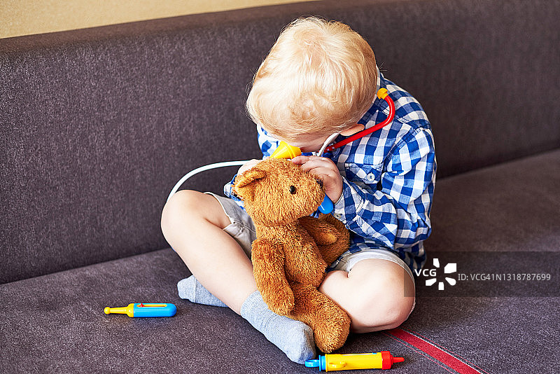 小男孩玩医生玩玩具工具和泰迪熊。图片素材
