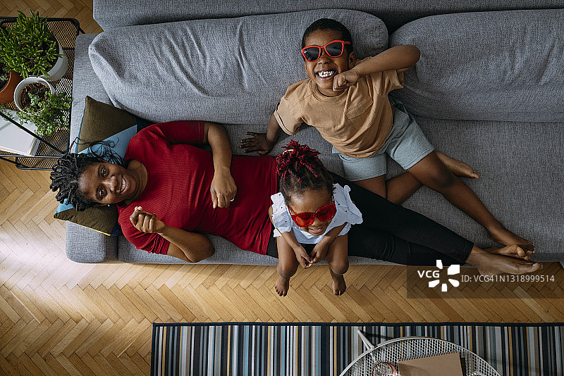 俯视图快乐的母亲放松和看着相机与她的女儿和儿子在沙发上图片素材