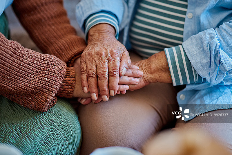 照片中，一个面目全非的女人和年长的亲戚手牵着手坐在家里的沙发上图片素材