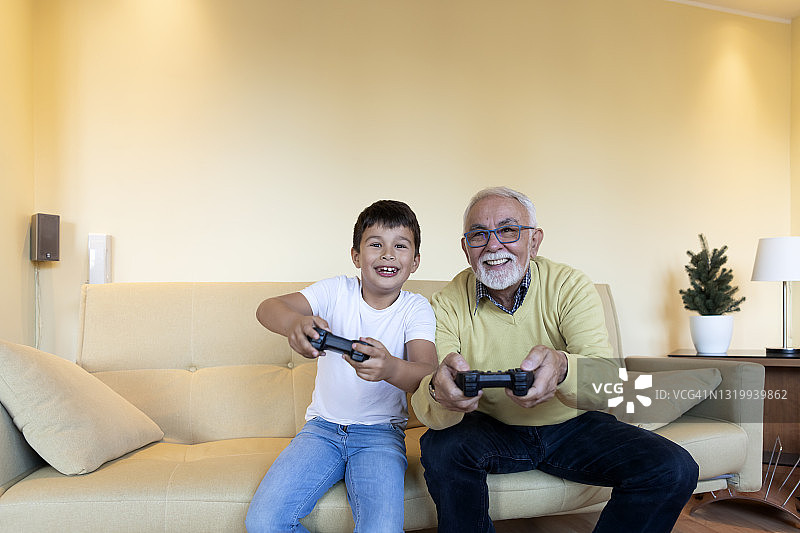 微笑的男孩和他的爷爷一起在家里玩电子游戏。图片素材
