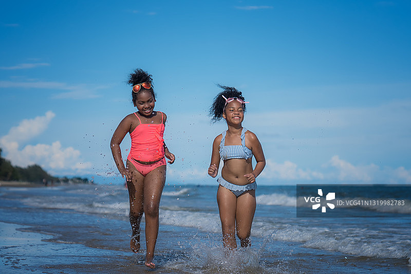 两个非洲裔美国孩子在海滩上跑步。图片素材