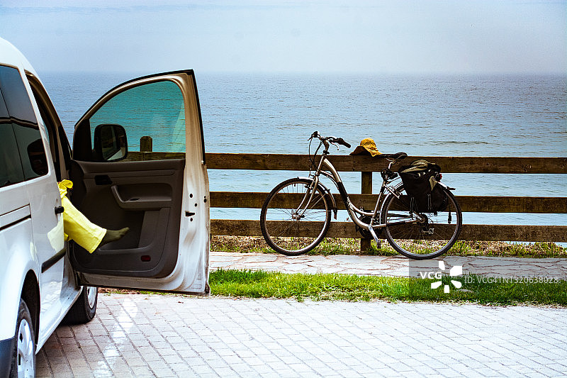 一辆白色面包车的侧视图，车门开在一个海滩的停车场。停车场里有一辆老式自行车。图片素材