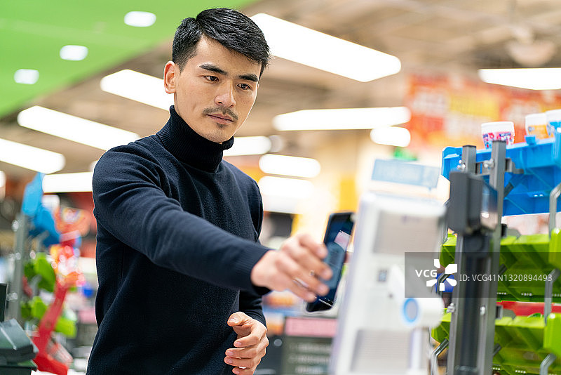 亚洲男性顾客用手机扫描非接触式自助支付的密码图片素材