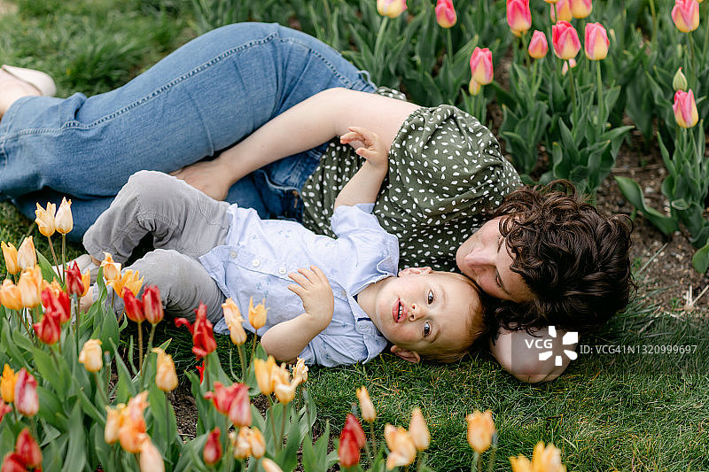 妈妈和蹒跚学步的儿子躺在郁金香花园的草地上图片素材