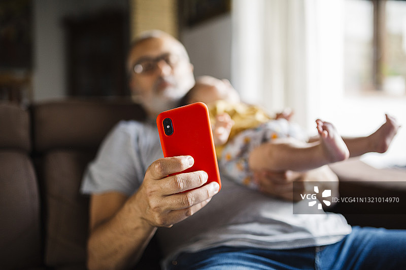 一个男人坐在沙发上和他的孩子看智能手机图片素材