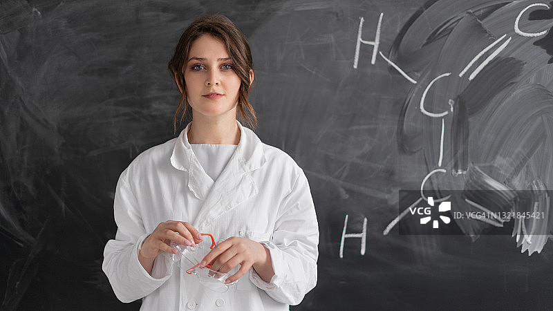 一位白种人女士站在一块写着化学公式的黑板前。化学老师或家教。概念回到学校。图片素材