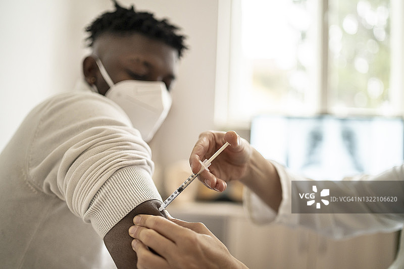 负责任的男患者看着医生在手臂注射COVID-19疫苗，并佩戴防护口罩图片素材