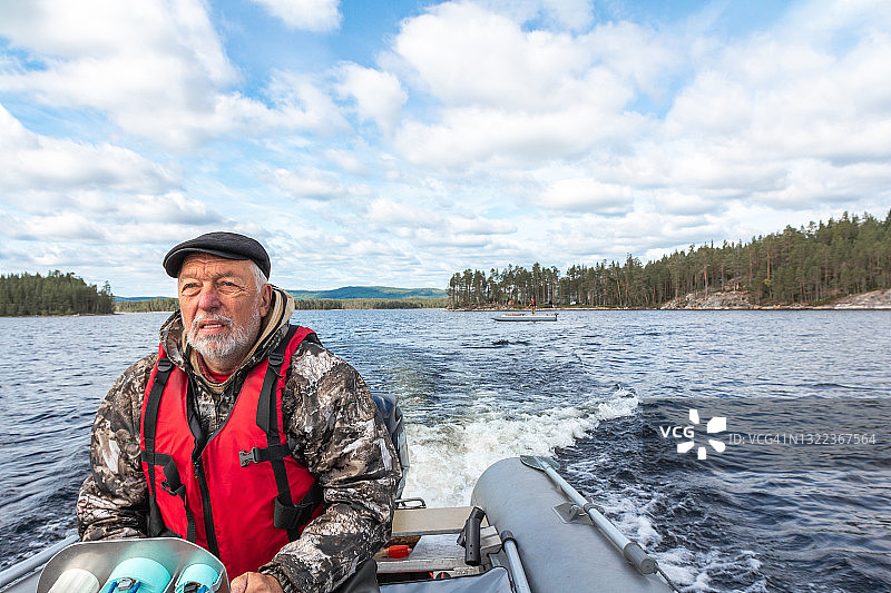 一位戴着帽子，穿着红色救生衣，留着灰色胡子的老人，在一个小岛上驾驶着一艘高速充气摩托艇图片素材
