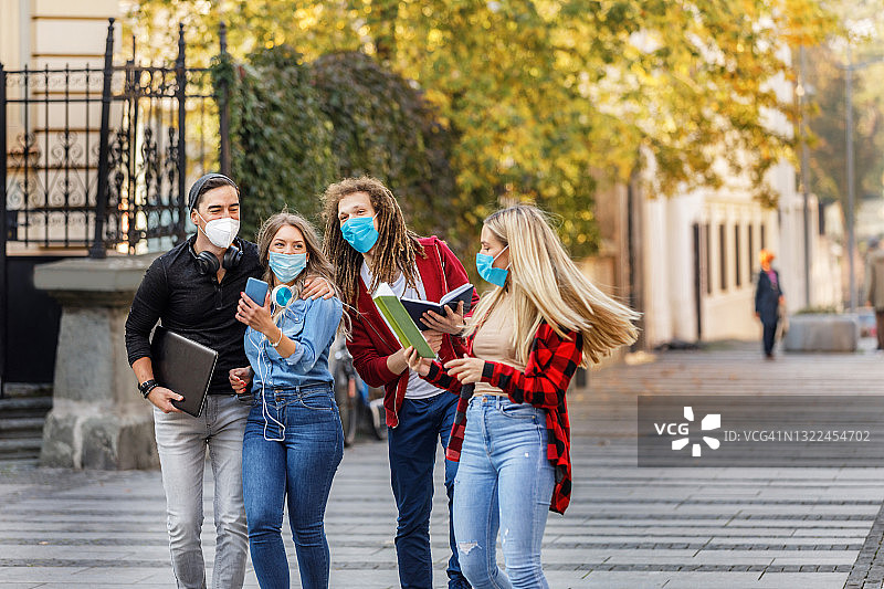 四个学生戴着防护口罩走在市区里。图片素材