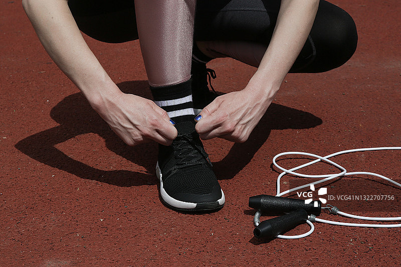 跑步鞋。在运动场上系鞋带的女人。跑步者为慢跑做准备。图片素材