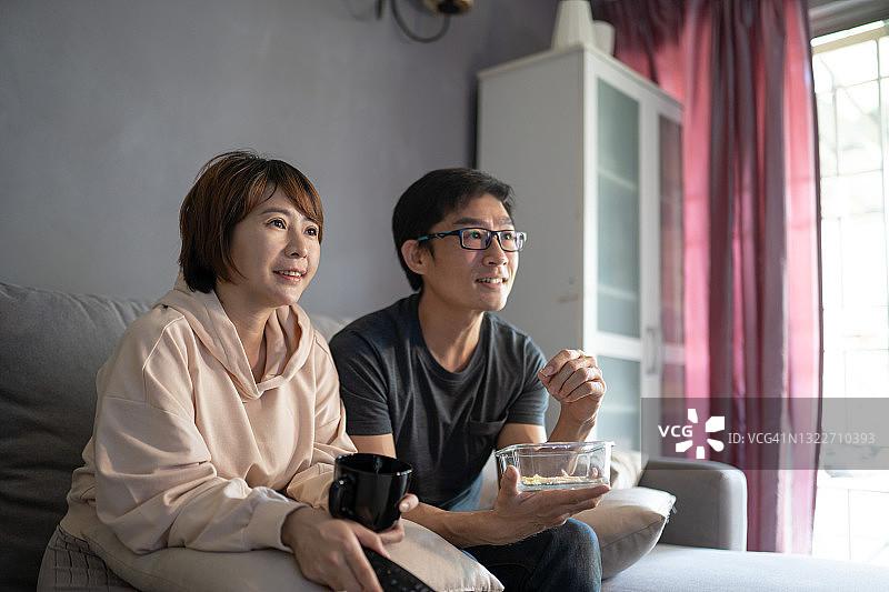 一对亚洲华人夫妇坐在沙发上看电视电影。图片素材