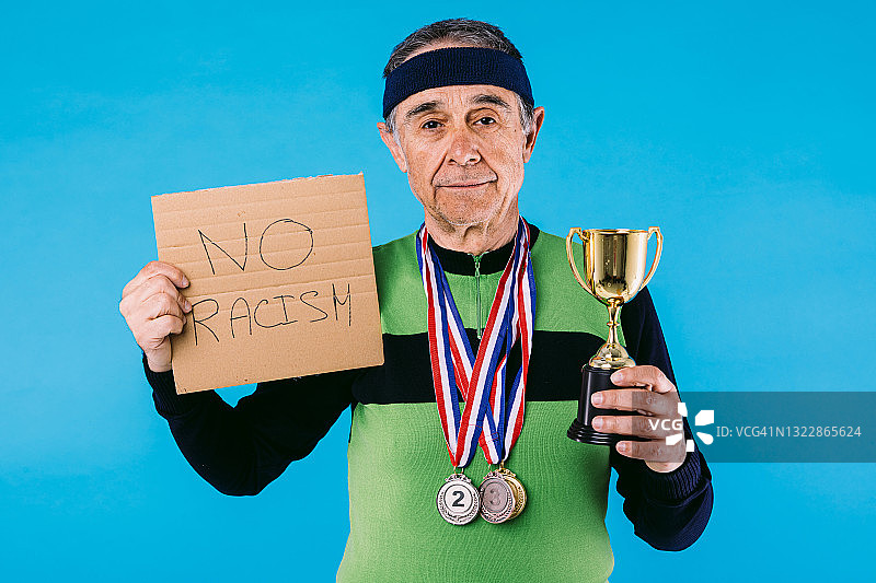 年长的运动员穿着绿黑相间的复古球衣，挂着3枚奖牌，上面写着:“反对种族主义”，另一只手拿着蓝色背景上的奖杯。图片素材