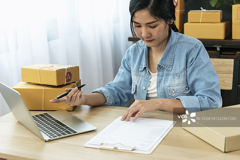 网上卖家双手合上年轻的亚洲女子敲击笔记本电脑键盘检查网上订单，检查货物库存发货包裹邮寄。亚洲女性在家创业图片素材