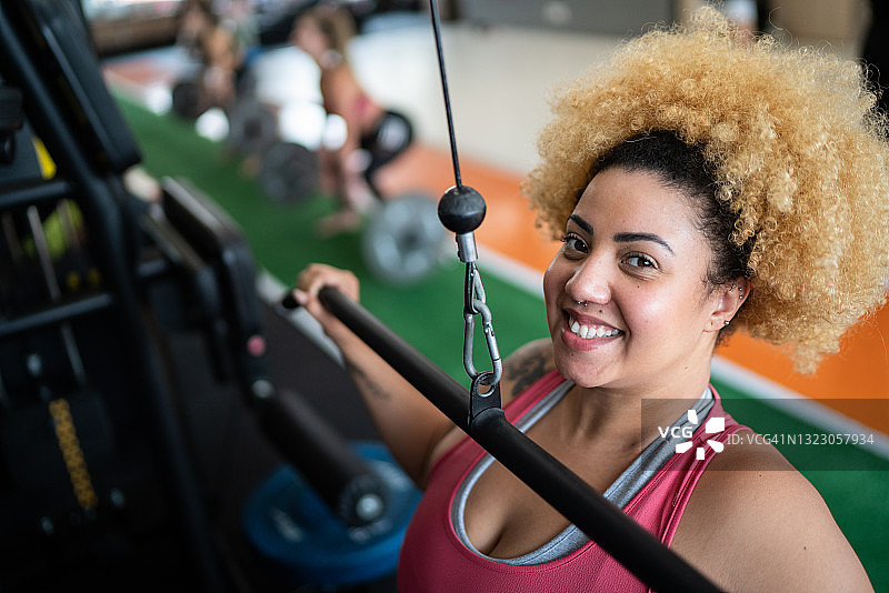 一个快乐的年轻女人在健身房拉举重机的肖像图片素材