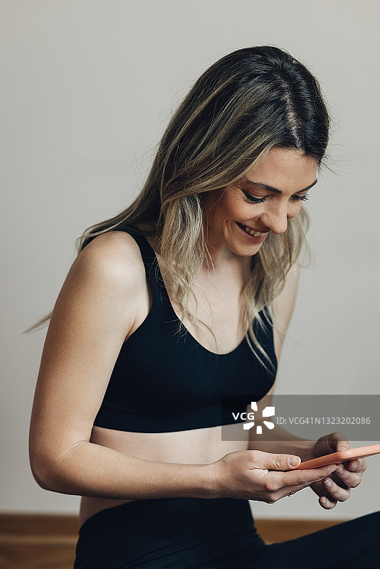 选择健身音乐:美丽微笑的女人坐着，在她的智能手机上设置播放列表图片素材