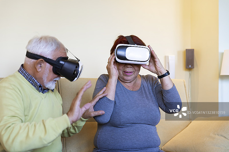 家中客厅里的老夫妇正戴着虚拟现实眼镜，用手做着手势。图片素材