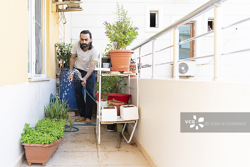关心和灌溉他在阳台上生长的植物的人。图片素材