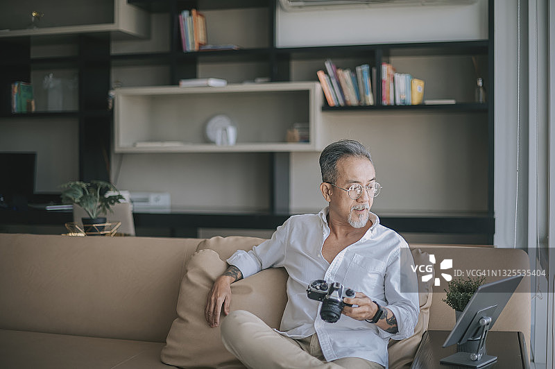 亚洲华人退休老人放松在客厅使用数字平板电脑，同时拿着他的相机检查他的图像转移图片素材