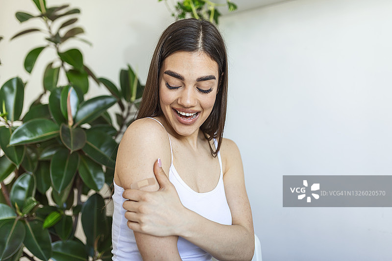 一名女子在接受covid-19疫苗接种后，用绷带指着自己的手臂。年轻女子接种冠状病毒疫苗后露出肩膀图片素材