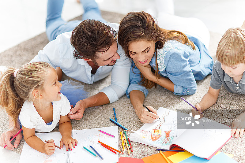 年轻的家庭在家里的地毯上放松的同时着色。图片素材