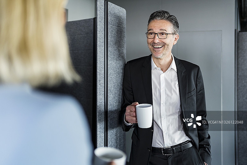 在办公室休息时间，拿着咖啡杯微笑的男企业家与女职业人士交谈图片素材